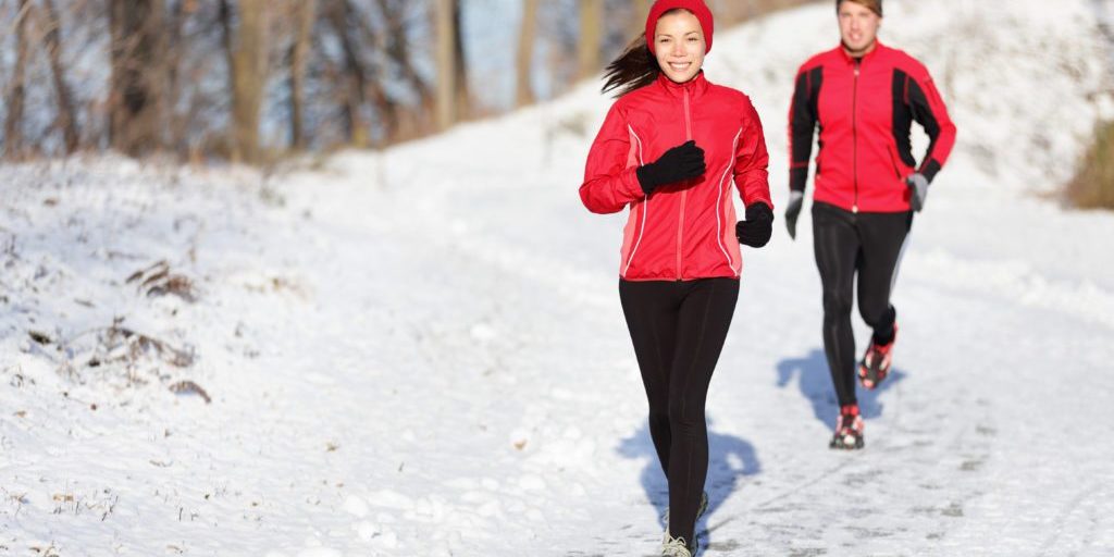 Winter running exercise couple. Runners jogging in snow. Young asian woman fitness model and caucasian man.Sport couple running in winter.