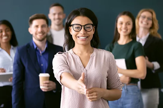 Image of a group of company employees with a woman in front holding out her hand for a handshake
