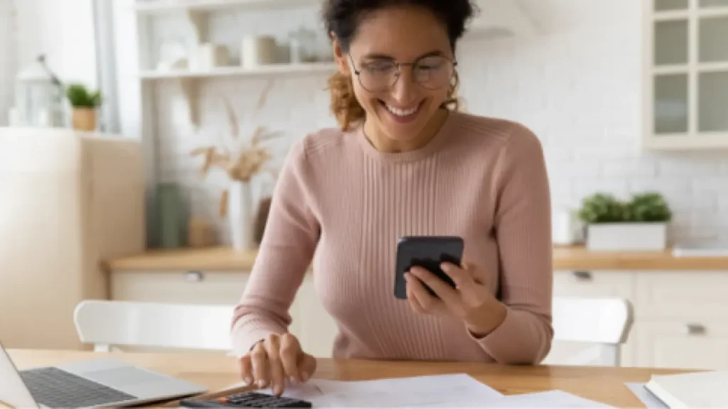 Woman sitting at her table looking at her calculator as she works on her budget.